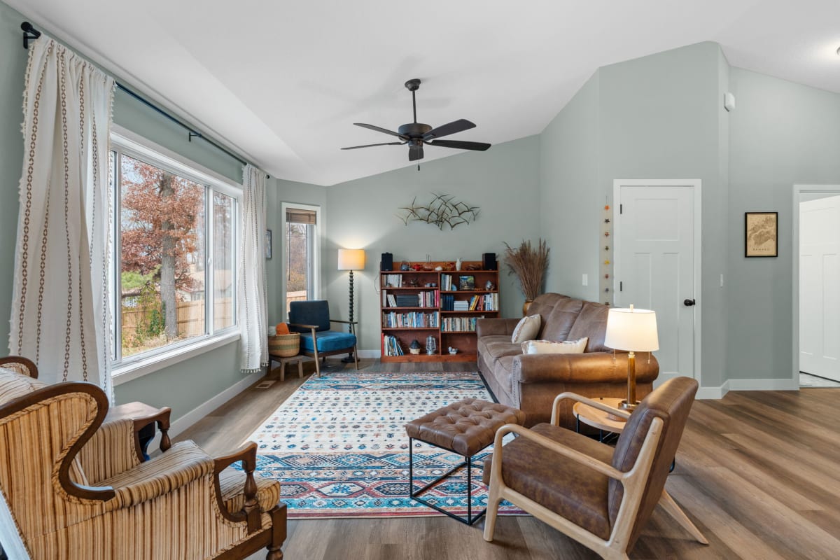 Unwind in your serene living space with comfortable leather seating, charming bookshelf library, and peaceful autumn views through large windows.