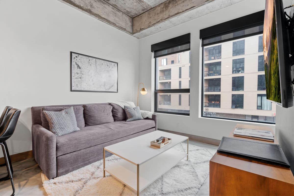 Unwind in your stylish living room with exposed beam ceilings, plush sofa, and city views through large windows.