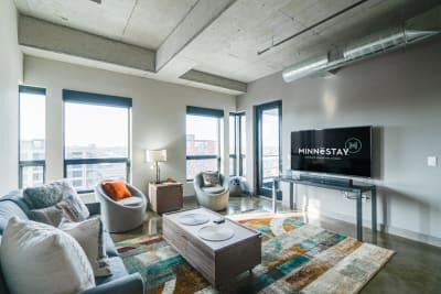 Modern living room with large windows, a gray sofa, an armchair, a coffee table, and a mounted TV.