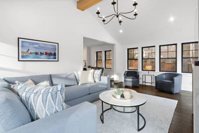 A bright living room featuring gray furniture, a round coffee table, and large black-framed windows.