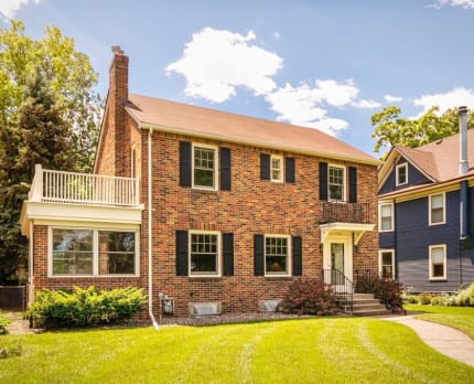 Front view of a charming brick colonial home with a balcony and green lawn.