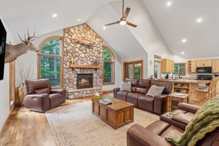 Cozy living room with stone fireplace and leather sofas, overlooking greenery.