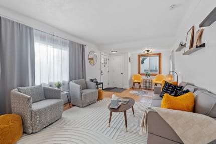 A cozy living room featuring a gray sofa, patterned armchairs, and bright yellow chairs, illuminated by natural light.