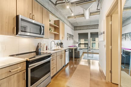 Modern kitchen with light wood cabinets and stainless steel appliances, leading to a cozy living area.
