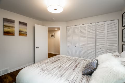 Modern bedroom with a bed, decorative pillows, abstract paintings, and a closet.