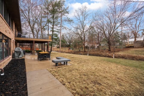 A residential backyard with a concrete patio, outdoor dining set, and trees.