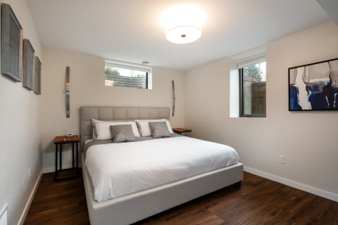 Modern bedroom featuring an upholstered bed, wooden nightstands, and large windows.