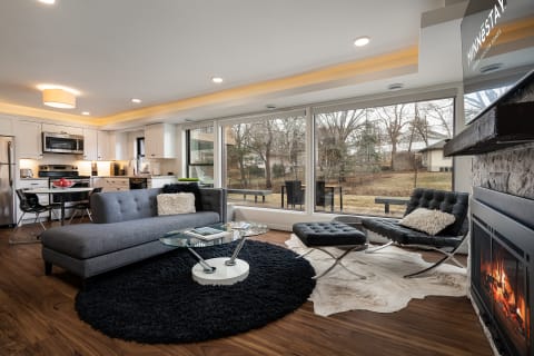 Stylish living room with gray sofa, black chairs, and large windows overlooking a natural landscape.