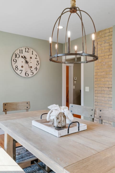 A dining room with a wooden table, metal chandelier, and wall clock.
