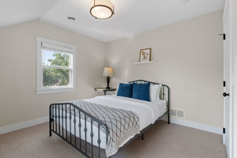 Cozy bedroom with a metal bed frame, decorative pillows, and natural light coming from a window.