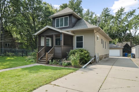 A charming two-story house with a porch, surrounded by greenery in a quiet neighborhood.
