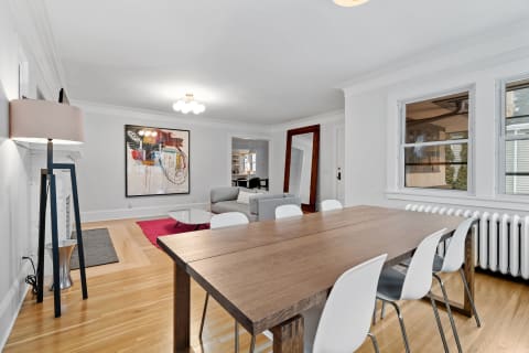 Contemporary dining and living room interior featuring a wooden table, white chairs, and an abstract painting.