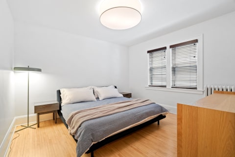 A serene bedroom with a large bed, bedside tables, a lamp, and wooden flooring.