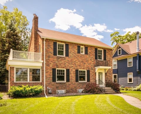 Front view of a charming brick colonial home with a balcony and green lawn.