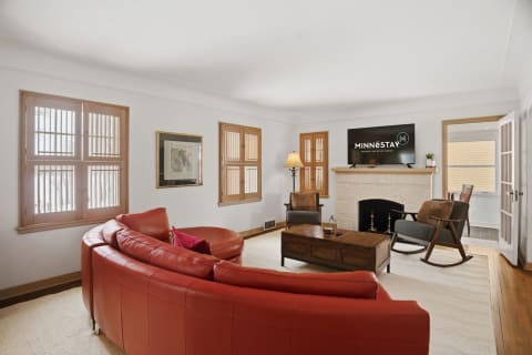 Bright living room with red leather sofa, wooden windows, and a cozy fireplace.