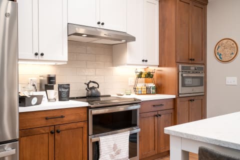 A contemporary kitchen featuring wooden and white cabinets, a stylish black kettle, and a wire basket of fruits.