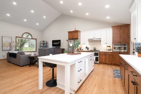A modern kitchen and living room with white and dark wood cabinetry, a large island, and a comfortable seating area.