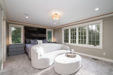 Spacious modern bedroom with upholstered bed, gray dresser, and white loveseat.