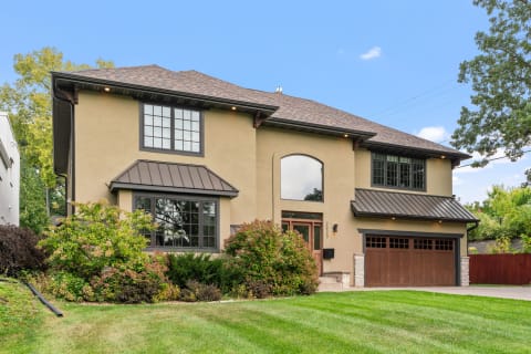 Modern house exterior with lush yard and dark metallic roofing.