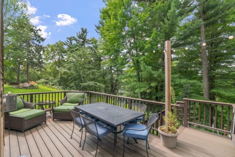 Outdoor deck with green seating and a dining table surrounded by trees.