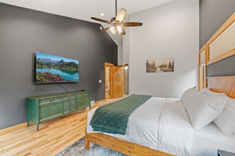 Modern bedroom featuring a flat-screen TV, a green dresser, and a large bed with white bedding.