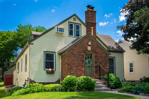 A cozy house with a green door, brick and stucco exterior, and lush gardens.
