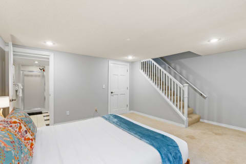 Cozy basement bedroom featuring a bed with colorful pillows and a stairway.