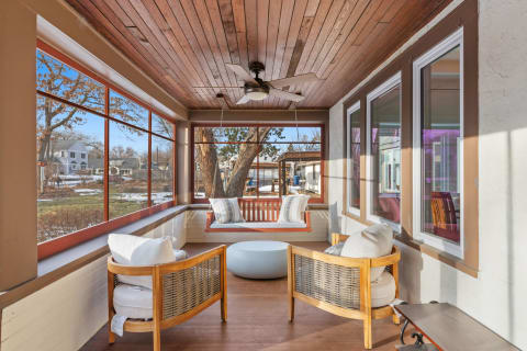 A cozy sun porch with a wooden ceiling, panoramic windows, and a swing seat.