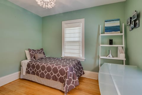 A small bedroom with a green wall, a bed with patterned bedding, and modern furniture.