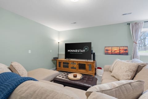 Cozy living room with beige sectional sofa, rustic cabinet, and large TV on light green wall.