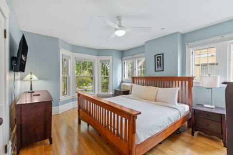 Serene bedroom with blue walls and wooden furniture, featuring a bed, nightstand, and windows.
