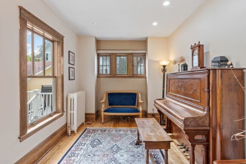 A room with a wooden piano, blue bench, and hardwood floor, illuminated by natural light.