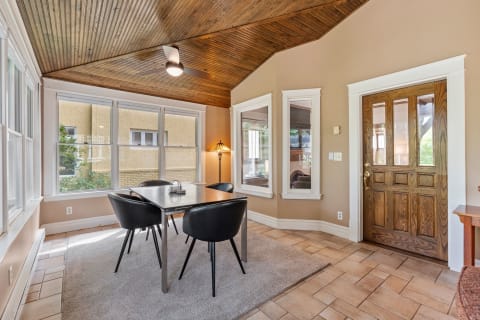 A cozy dining space featuring a rectangular table, black chairs, large windows, and wooden ceiling.