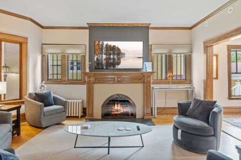 A warm living room with a fireplace, TV above the mantel, and cozy gray armchairs.