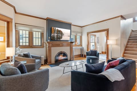 A stylish living room featuring a modern marble coffee table, navy sofa, and a fireplace with a large TV displaying a nature scene.