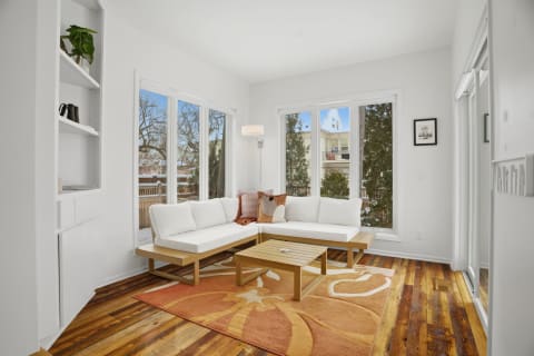 Cozy corner seating area with a white sectional couch and wooden coffee table in a sunlit room.