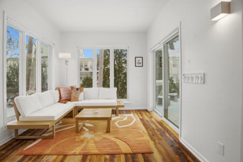 Bright living room with white sectional couch, wooden coffee table, and large windows with a view of trees outside.