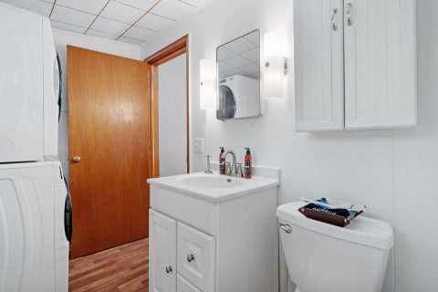 Compact bathroom with a washer and dryer, sink, and wooden door.