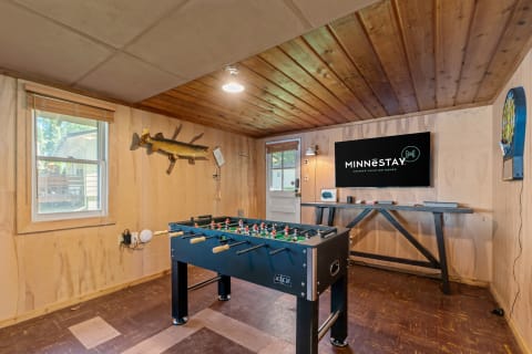 A game room with a foosball table and a TV displaying the MINNESTAY logo.
