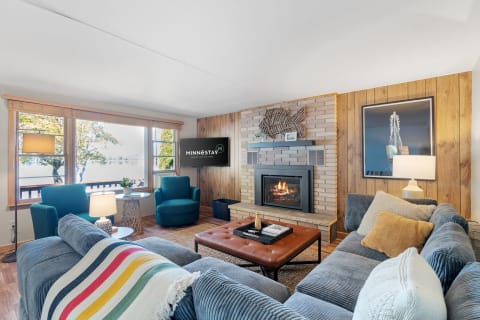 Inviting living room with a sectional sofa, fireplace, and large windows overlooking trees and water.