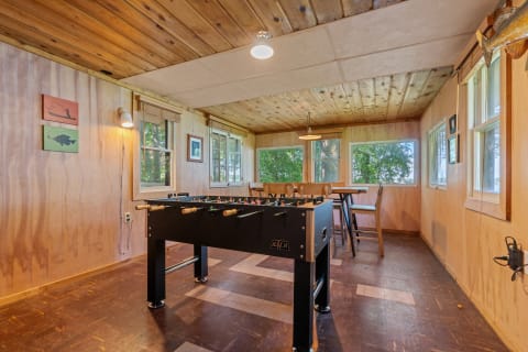 Interior of a rustic game room featuring a foosball table and wooden dining furniture.