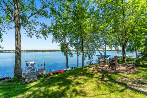 Lakeside view with dock, chairs, and kayak on a sunny day.