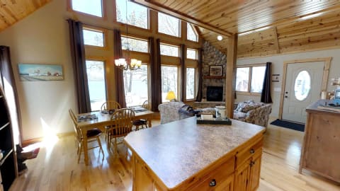 Interior view of a rustic cabin, featuring a dining table, living area, and large windows.