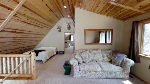 A rustic loft bedroom featuring a floral couch, wooden ceiling, and deer head mounts.