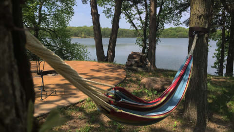 A colorful hammock hanging between trees near a tranquil lake.
