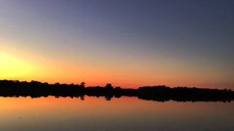 A tranquil sunset over a lake, with vibrant colors and tree silhouettes.