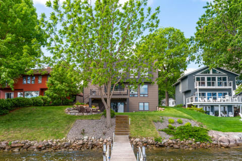Two modern homes by a lake, featuring a wooden dock and abundant greenery.