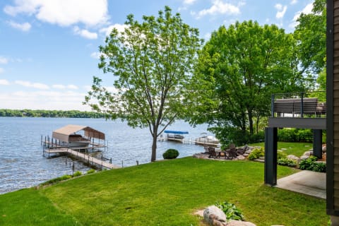 Lakeside view with dock, boat slip, fire pit, and green lawns under a blue sky.