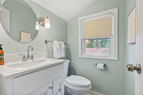 Modern bathroom with green walls, white vanity, and natural light.
