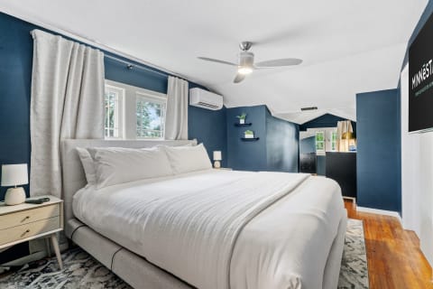 A stylish bedroom featuring navy walls, a white bed, and natural light from windows.